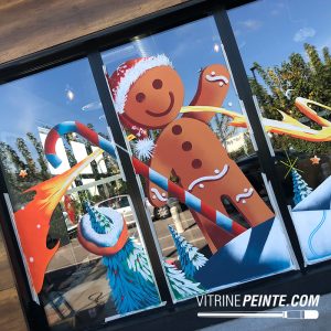 Peinture sur vitrine de Noël représentant un Pain d’épice géant dans un décor gourmand