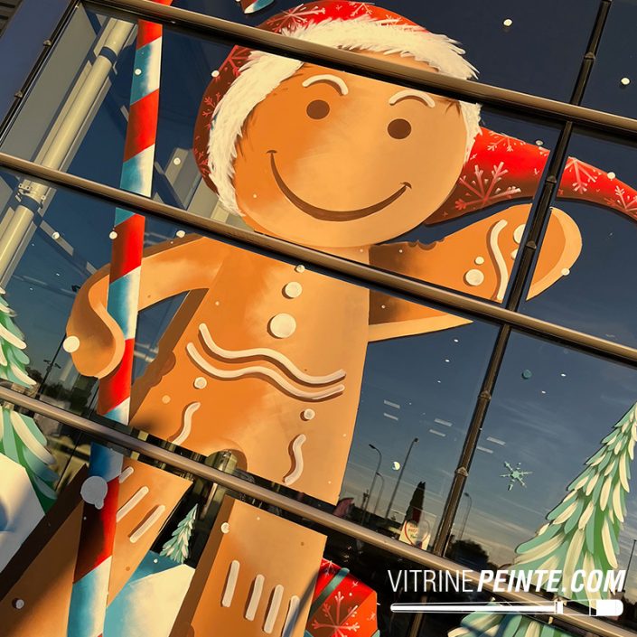 Décoration de vitrine de Noël peinte à la main avec un bonhomme en pain d’épice géant sur la vitrine d’une concession automobile.