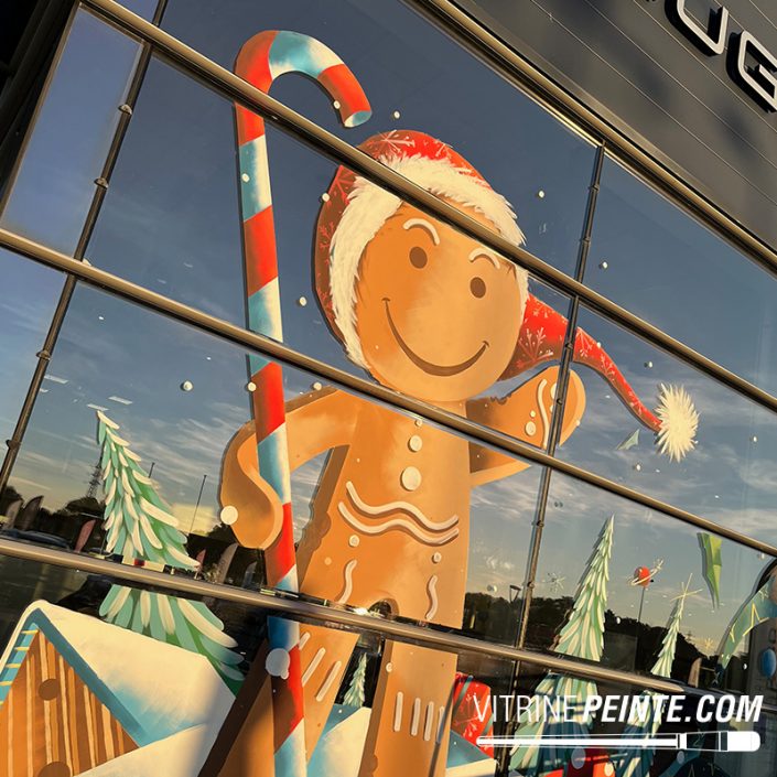Décoration de Noël sur vitrine de concession automobile avec un bonhomme en pain d’épice géant, peinture décorative réalisée sur mesure.